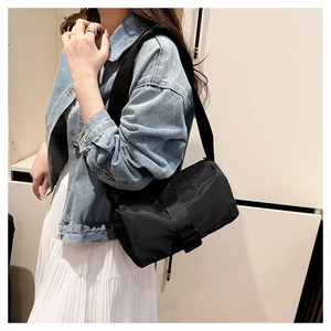 Close-up of black nylon crossbody bag with wide shoulder strap worn with casual outfit
