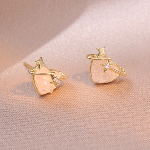 Macro view of pink heart stone earrings with golden star orbital ring on satin
