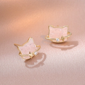 Macro shot of pink cat planet stud earrings with gold orbit rings on champagne silk