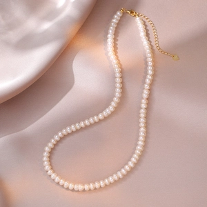 Detail of freshwater pearl necklace with gold lobster clasp on silk fabric background