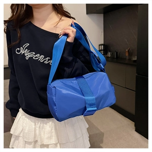 Detail of bright blue cylindrical nylon crossbody bag worn over shoulder by model