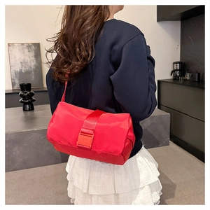 Close-up of a vibrant red nylon crossbody bag with large buckle on a model wearing white skirt