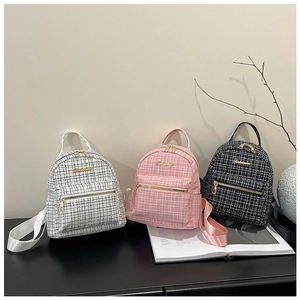 Trois mini sacs à dos en tweed de couleurs blanc, rose et noir sur un support moderne