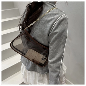Close-up of a clear PVC shoulder bag with brown leather trim and a gold chain strap