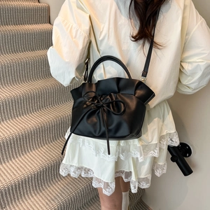 Sac à main noir en cuir à volants avec nœud, porté par un mannequin dans un décor élégant
