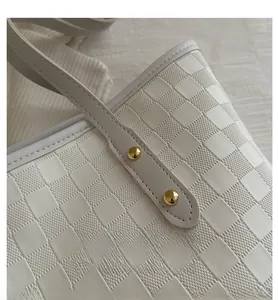 Detailed close-up of textured checkered pattern on cream tote bag with gold rivets
