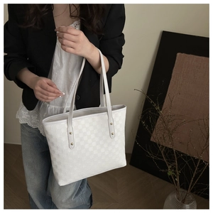 Detail of white quilted tote bag featuring checkered texture and gold metal rivet accents