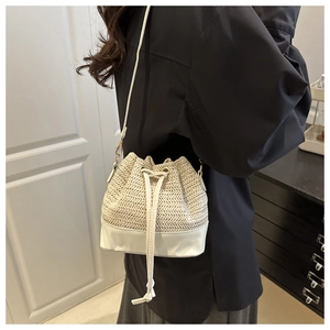 Detail of woven straw bucket bag with white faux leather base and drawstring closure