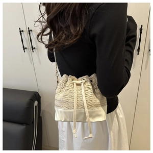 Detail of a straw drawstring bucket bag with white leather straps and textured weaving