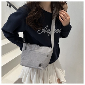 Detail of light grey nylon crossbody bag with zipper pocket and metal logo on a model