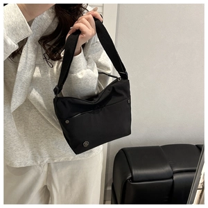 Detalle de bolso bandolera de nailon negro con correa ancha ajustable y logotipo M metálico