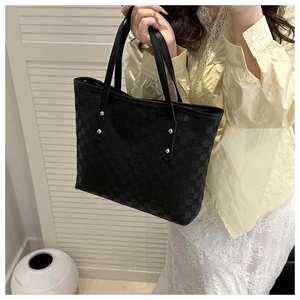 Detail of black quilted tote bag featuring golden rivet hardware and leather handles