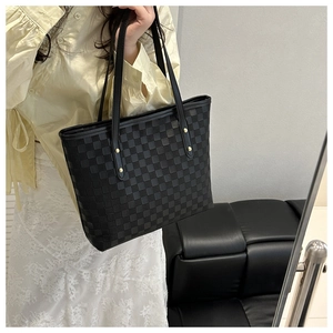 Detail of black quilted tote bag with woven texture and thin leather handles on a model