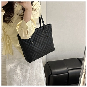 Detail of black checkered tote bag with slim shoulder straps worn by a model