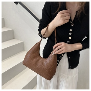 Brown woven hobo bag styled with a white pleated skirt and black cardigan on stairs
