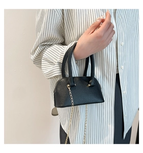 Close-up of black lychee grain leather shell bag with golden chain strap and handle