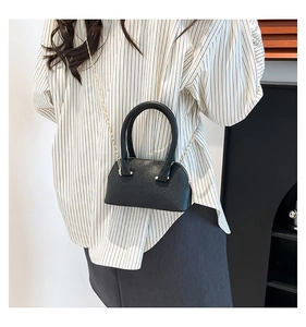 Modern black shell bag with lychee texture and gold chain strap shown on a model
