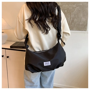 Detail of black nylon shoulder bag with ruffled strap and Fashion label on white background