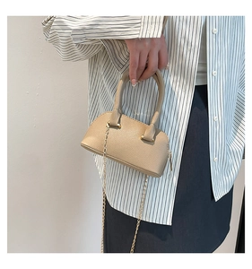 Detail of beige textured leather shell bag with gold chain strap held by model