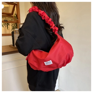 Detail of red pleated shoulder strap and brand label on a stylish oversized hobo bag