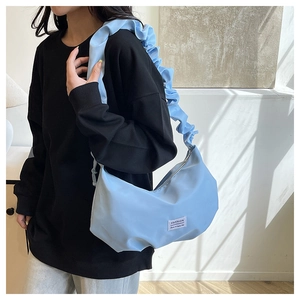 Detail of light blue crescent bag with ruffled strap and fashion brand label