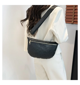 Detail of black woven texture crossbody bag with gold zipper and wide strap on white suit