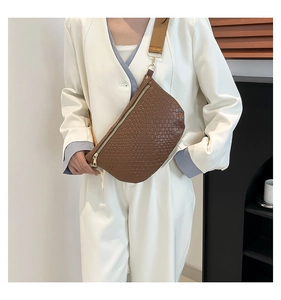 Close-up of brown woven texture crossbody bag with wide canvas strap worn by a model