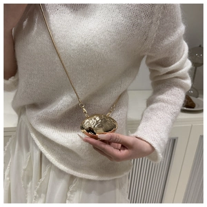 Macro detail of glossy gold shell-shaped crossbody bag with slim gold chain strap on model