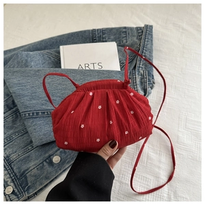 Detail of red pleated mini crossbody bag with white floral embroidery and thin strap