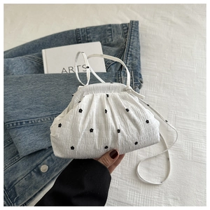 Close-up of a white pleated cloud bag with black flower embroidery and slender straps