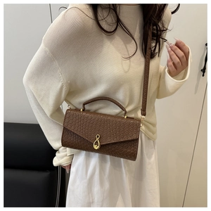 Detail of woven texture shoulder bag with gold treble clef buckle on a model
