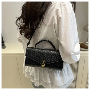 Detail of black crocodile texture handbag with golden water drop clasp on white outfit