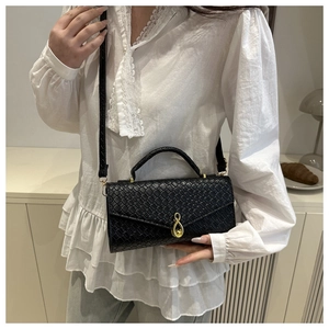 Detail of black woven texture handbag featuring a gold teardrop clasp and leather handle