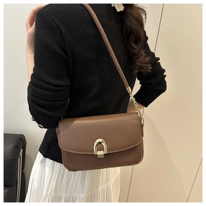 Detail of a brown leather shoulder bag with a gold horseshoe buckle on the side profile
