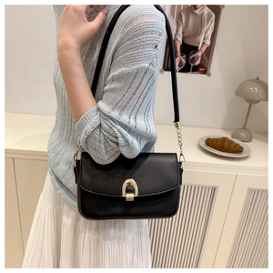 Detail of a vintage black leather crossbody bag featuring a golden horseshoe magnetic buckle