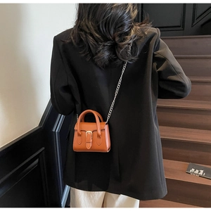 Mini caramel brown square crossbody bag shown on a model against dark steps