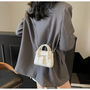 Close-up of white mini handbag with metal chain and leather buckle on a grey blazer