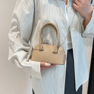 Minimalist beige shell bag with litchi texture and gold chain strap worn by a model