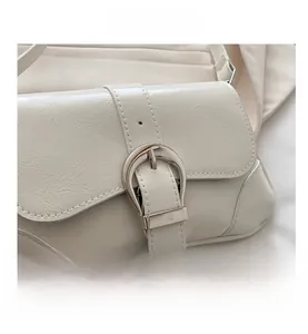 Detail of off-white wrinkled PU leather saddle bag featuring a silver horseshoe buckle