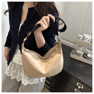 Detail of beige crescent dumpling bag with black adjustable strap and golden hardware