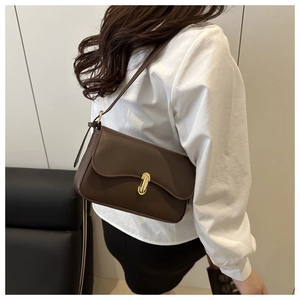Close-up of a dark brown leather shoulder bag featuring an oval gold buckle on a model
