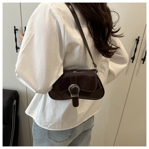 Detailed view of deep brown saddle bag with large silver buckle on model's shoulder