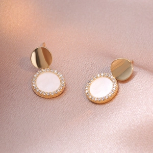 Boucles d'oreilles dorées en nacre et cristaux sur fond de satin rose soyeux