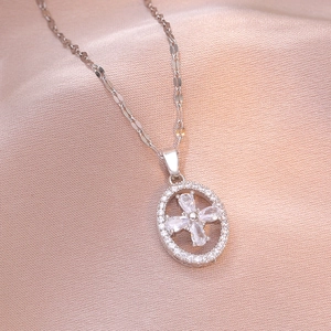 Silver tone oval pendant necklace with four-leaf zircon flower on pink fabric