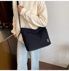 Detail of black crossbody bag featuring a woven rope strap and white IU logo accent