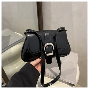 Detail of glossy black shoulder bag featuring a large silver D-buckle and adjustable strap