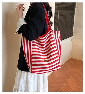 Detail of red and white striped canvas tote bag featuring a metallic logo and red straps