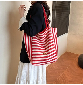 Detail of a large red and white striped tote bag showing modern shoulder style on a model