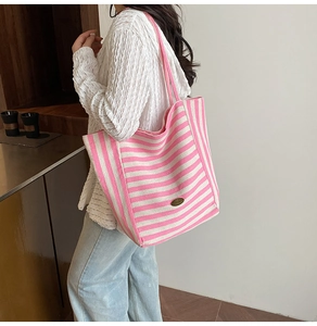 Close-up of pink striped tote bag with leather strap and metal logo plate on textured canvas