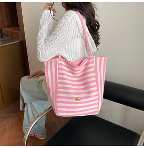 Detail of pink and white striped canvas tote bag showing the metal logo and sturdy handles